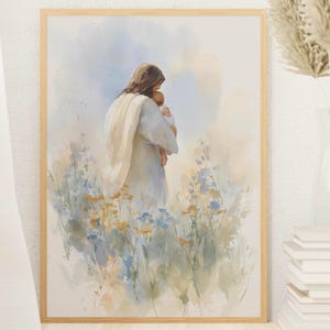 May include: Watercolor print in a light wooden frame. The artwork depicts a figure in white robes holding a baby, surrounded by wildflowers in a field. The color palette includes soft blues, yellows, and greens, with a light blue sky in the background.