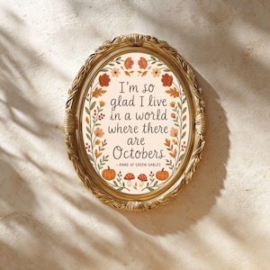 Puede incluir: Un marco ovalado de tono dorado que contiene una impresión con el texto "I'm so glad I live in a world where there are Octobers - Anne of Green Gables". La impresión presenta un borde de flores, hojas, calabazas y setas naranjas, rojas y verdes.