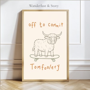 May include: A framed wall art print featuring a line drawing of a shaggy highland cow standing on a skateboard. The text above reads "off to commit" and the text below reads "Tomfoolery" in orange. The brand name "Wanderlust & Story" is at the top.