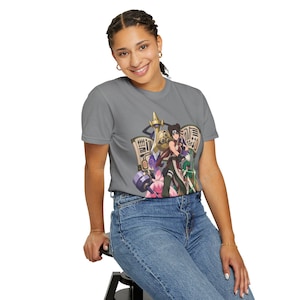 May include: A grey short-sleeve t-shirt featuring a graphic print of an anime character with dark hair, wearing a dark outfit, surrounded by various weapons, scrolls, and a pink creature, paired with blue denim jeans.