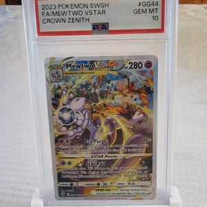 Puede incluir: Una carta Pok&eacute;mon de Mewtwo VSTAR del set Crown Zenith, calificada y protegida en un estuche. La carta est&aacute; calificada como GEM MT 10. La ilustraci&oacute;n presenta a Mewtwo en una pose din&aacute;mica, con colores morados y naranjas.