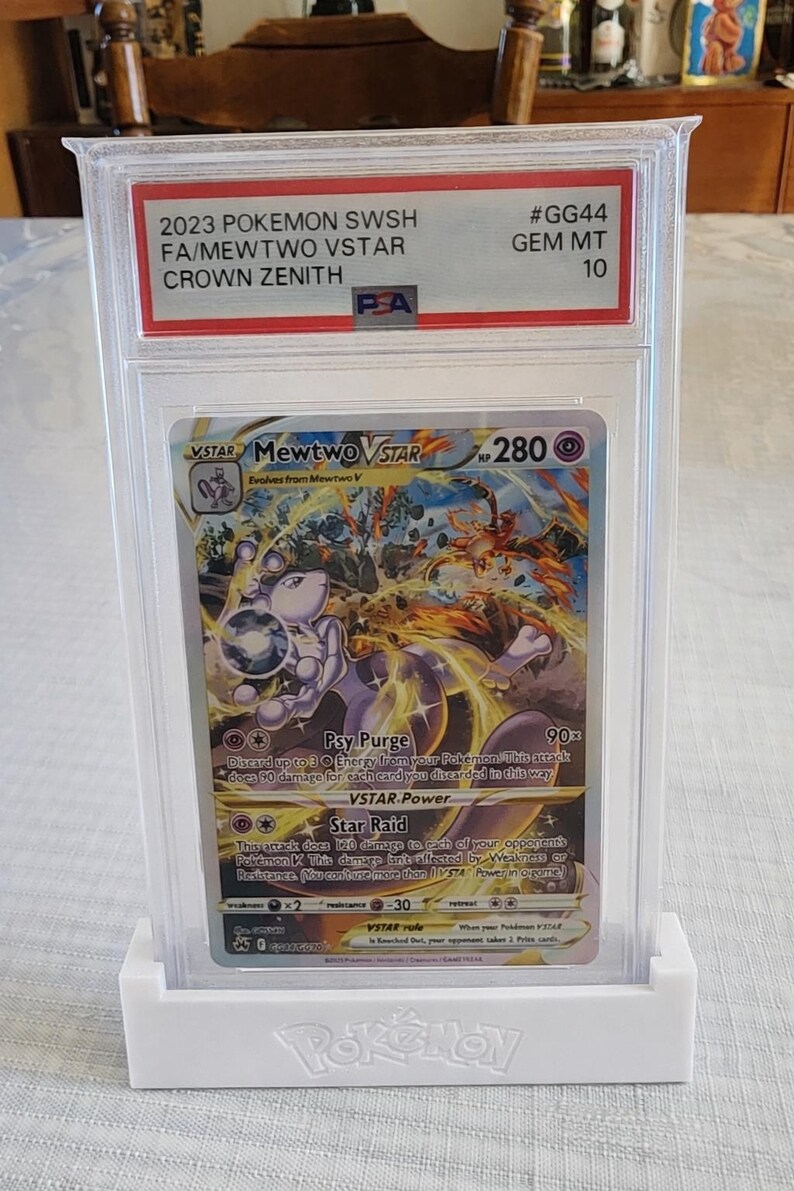 Puede incluir: Una carta Pok&eacute;mon de Mewtwo VSTAR del set Crown Zenith, calificada y protegida en un estuche. La carta est&aacute; calificada como GEM MT 10. La ilustraci&oacute;n presenta a Mewtwo en una pose din&aacute;mica, con colores morados y naranjas.