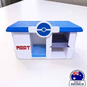 以下が含まれることがあります： 青い屋根と赤い「MART」の文字が入った、白と青のプラスチック製の収納ボックス。前面には青と白の円形ロゴがあります。このボックスは建物に似せてデザインされています。