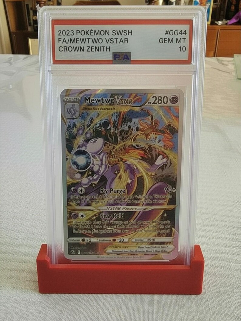 Puede incluir: Una carta Pok&eacute;mon Mewtwo VSTAR calificada del set 2023 Pok&eacute;mon SWSH Crown Zenith. La carta est&aacute; encapsulada en un soporte protector transparente y se muestra en un soporte rojo. La carta tiene una colorida ilustraci&oacute;n de Mewtwo.