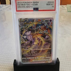 Puede incluir: Una tarjeta Pok&eacute;mon de 2023, calificada, con Mewtwo VSTAR del conjunto Crown Zenith. La tarjeta est&aacute; encerrada en un soporte protector con una base negra. La tarjeta contiene el texto "2023 POKEMON SWSH FA/MEWTWO VSTAR CROWN ZENITH".