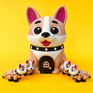 Op de afbeelding: Een grillig hondenbeeldje met een huisvormige deur, omringd door kleinere hondenfiguren. De grote hond is bruin, wit en roze, met een zwarte halsband. De achtergrond is helder geel. De kleinere honden hebben beweeglijke ledematen.