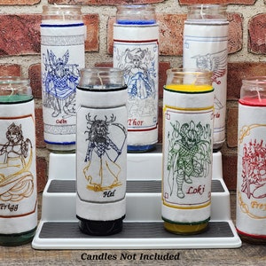 May include: Embroidered candle sleeves depicting Norse deities such as Odin, Thor, and Loki. The white sleeves have detailed embroidery in various colours, with the figures' names below. The image also includes the text "Candles Not Included."