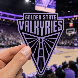 May include: A triangular sticker featuring the text GOLDEN STATE VALKYRIES in bold purple lettering on a black background. The design includes a stylized bridge graphic pointing downward, framed by a purple border, creating a sharp geometric emblem.