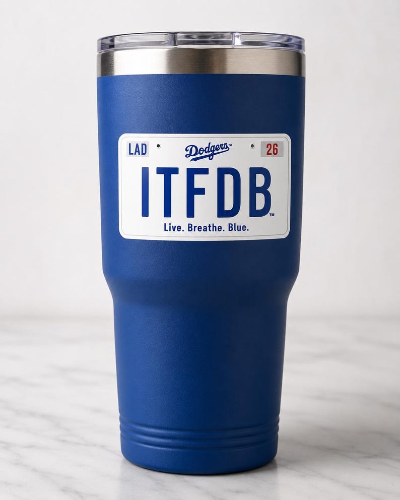 May include: A royal blue stainless steel tumbler with a clear lid and a white rectangular graphic resembling a license plate. The graphic features the text LAD, Dodgers, 26, ITFDB, and the phrase Live. Breathe. Blue. in blue and red lettering.