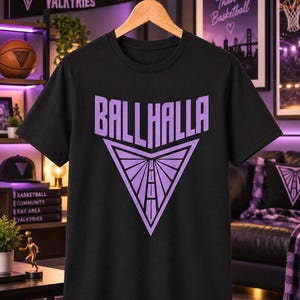 May include: A black short-sleeve t-shirt featuring a light purple graphic print on the chest. The design displays the text BALLHALLA above a triangular emblem containing a stylized road leading toward a horizon point with radiating lines.