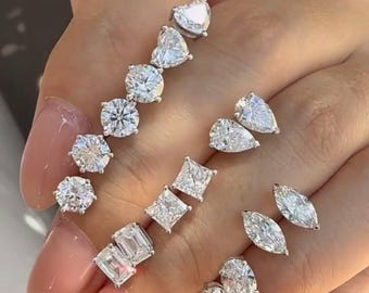 Puede incluir: Una colección de pendientes de botón en tono plateado con varios cortes de piedras preciosas transparentes, incluyendo formas de corazón, redonda, pera, cuadrada, esmeralda, marquesa y ovalada, dispuestas en filas para mostrar los diseños.