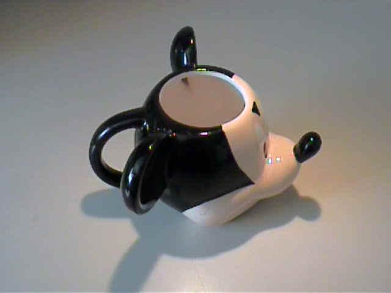 May include: A ceramic mug shaped like the head of a cartoon mouse. The mug features a glossy black and white color scheme, large rounded ears, a protruding snout with a small black nose, and a curved handle attached to the back of the head.