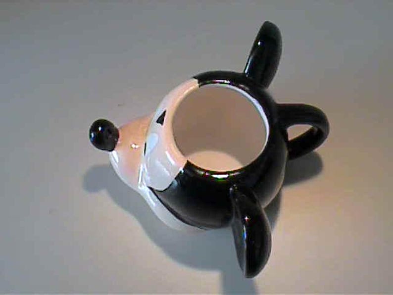 May include: A ceramic mug shaped like a cartoon mouse head, featuring a glossy black and white finish. The mug has a rounded body, a protruding snout with a black nose, two large black ears, and a small handle on the side for holding.