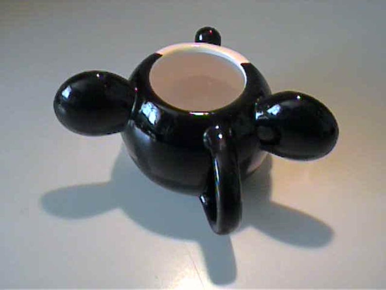 May include: A glossy black ceramic mug featuring a rounded body with three protruding, bulbous black handles extending from the sides. The interior of the mug is white, and the top rim is also white, contrasting with the dark exterior finish.