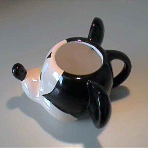 May include: A ceramic mug shaped like a cartoon mouse head, featuring a glossy black and white finish. The mug has a prominent snout with a black nose, two large rounded ears, and a small handle on the back. The interior of the mug is white.