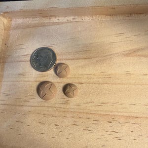 May include: Three small, tan-coloured, round buttons with a four-petal flower design are displayed next to a U.S. dime. The buttons vary in size, with the largest button approximately the same size as the dime.