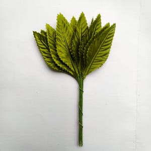 May include: A bundle of artificial green leaves with a textured surface. The leaves are arranged in a fan shape and are attached to a green wire stem. The leaves are a vibrant shade of green.