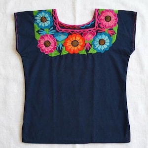 Op de afbeelding: Een donkerblauwe blouse met korte mouwen en een vierkante halslijn, versierd met levendig, meerkleurig bloemenborduurwerk. Het ontwerp bevat felroze, oranje en lichtblauwe bloemen met groene bladeren en een roze gestikte rand.