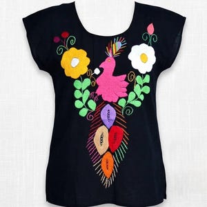 Peut inclure: Un haut noir à manches courtes orné d'une broderie colorée sur le devant. Le motif représente un oiseau rose central avec une crête multicolore, entouré de fleurs jaunes et blanches, de feuilles vertes et d'une queue aux motifs variés.