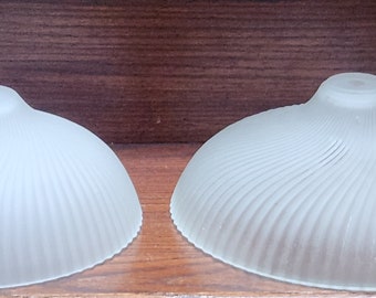 Puede incluir: Dos pantallas de lámpara de vidrio blanco esmerilado con un diseño acanalado. Las pantallas de lámpara están sobre una superficie de madera.