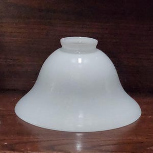 Peut inclure: Un abat-jour en verre blanc en forme de cloche, avec un dessus arrondi et un fond évasé. L'abat-jour a un aspect lisse et dépoli et est conçu pour diffuser la lumière. Il s'agit probablement d'un élément de remplacement ou décoratif pour une lampe.