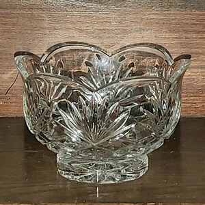 May include: A clear glass bowl with a scalloped rim and intricate cut-glass design. The bowl has a footed base.