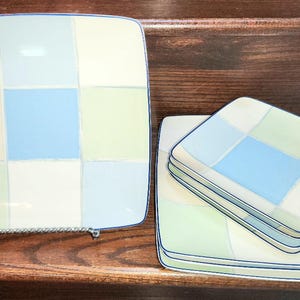 Può includere: Set di quattro piatti quadrati in ceramica con un motivo a scacchi in tonalità di blu, verde e bianco. I piatti hanno un bordo blu e sono impilati uno sopra l'altro.