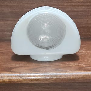 May include: A semi-circular white glass light fixture shade featuring a central clear glass lens with a concentric ribbed pattern. The shade has a smooth, opaque white finish and a rounded top edge, designed to be mounted on a circular base.
