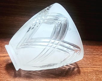 May include: A frosted glass decorative object with a geometric diamond pattern. The object has a triangular shape with a flat base and is resting on a wooden surface. The glass has a frosted appearance, and the diamond pattern is etched into the surface.