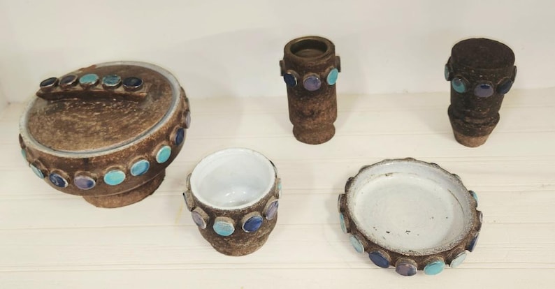 May include: A collection of brown ceramic pottery pieces, including a lidded jar, a small vase, a cup, a dish, and a cylindrical container. Each piece is adorned with turquoise and purple circular accents.