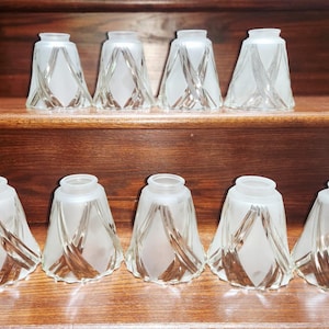 Peut inclure: Un ensemble de neuf abat-jours en verre en forme de cloche avec une finition dépolie et des lignes diagonales transparentes qui se croisent pour former un motif en losange. Chaque abat-jour a une ouverture circulaire en haut et en bas.