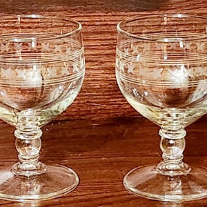 May include: Two clear glass wine glasses with etched designs. The glasses have a round bowl and a stem with a round base.