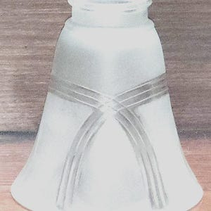 Könnte beinhalten: Lampenschirm aus mattiertem Glas mit einer ausgestellten, glockenförmigen Form. Der Schirm hat ein dekoratives Design aus sich kreuzenden Linien in der Mitte. Die Oberseite hat eine zylindrische Öffnung. Das Design ist schlicht und elegant.