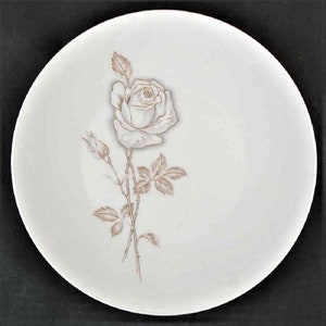 Puede incluir: Un plato de cerámica blanco con un contorno marrón de una sola rosa con hojas y tallos.