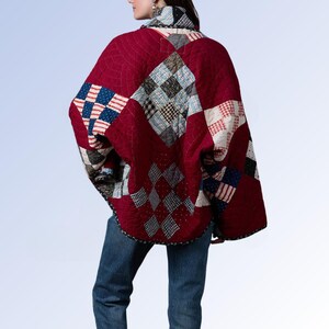 May include: A quilted jacket featuring a patchwork design with deep red fabric and various patterned squares in blue, white, and black. The garment has a high collar, long sleeves, and a loose, draped fit, paired with blue denim jeans.