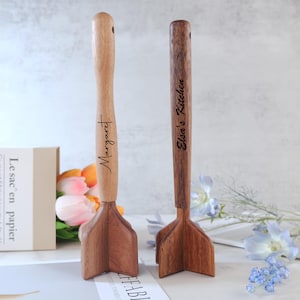 May include: Two wooden muddlers for the kitchen. One is light-toned with "Margaret" engraved on the handle. The other is dark-toned with "Elsa's Kitchen" engraved. Both have a hole at the top of the handle.