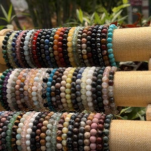 May include: A display of beaded bracelets in various colors, including green, black, red, and turquoise. The bracelets are made of small, round beads and are arranged on a multi-tiered display stand.