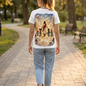May include: White t-shirt featuring a colorful illustration of a religious figure leading children through clouds. The design includes a blue sky, hot air balloons, and other whimsical elements. The shirt is made of a soft material.
