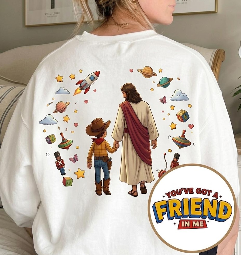 May include: White sweatshirt featuring a colorful graphic of Jesus holding hands with a cowboy, surrounded by planets, stars, and toys. The text "YOU'VE GOT A FRIEND IN ME" is in a circular design on the lower right.