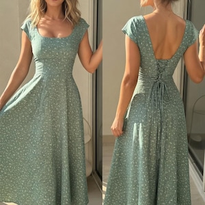 Könnte beinhalten: Ein salbeigrünes Midikleid mit quadratischem Ausschnitt und kurzen Ärmeln. Das Kleid hat ein Blumenmuster und ein figurbetontes Oberteil, das in einen ausgestellten Rock übergeht. Der Rücken des Kleides hat ein Schnürdetail. Das Model trägt eine Sonnenbrille.