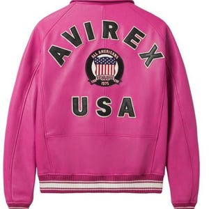 May include: A vibrant pink leather jacket with the word "AVIREX" arched across the back in black lettering. Below, a patch reads "ALL AMERICANS ESTABLISHED 1975 USA". The jacket has a collar, ribbed cuffs, and a white and black striped hem.