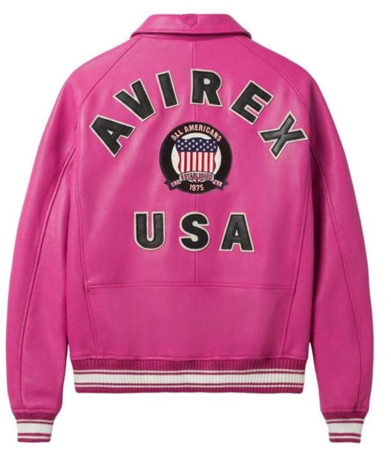 May include: A vibrant pink leather jacket with the word "AVIREX" arched across the back in black lettering. Below, a patch reads "ALL AMERICANS ESTABLISHED 1975 USA". The jacket has a collar, ribbed cuffs, and a white and black striped hem.