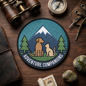May include: Embroidered patch featuring a dog and cat sitting in front of a mountain and trees. The patch is circular with the words "ADVENTURE COMPANIONS" in white lettering. The background is teal and blue.