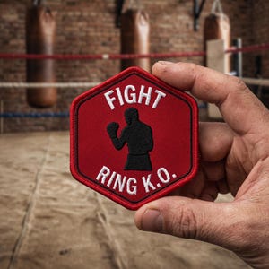 Könnte beinhalten: Ein sechseckiger gestickter Aufnäher mit rotem Hintergrund und einer schwarzen Silhouette eines Boxers in der Mitte. Der weiße Text lautet FIGHT über der Figur und RING K.O. darunter. Der Aufnäher hat einen roten gestickten Rand am gesamten Rand.