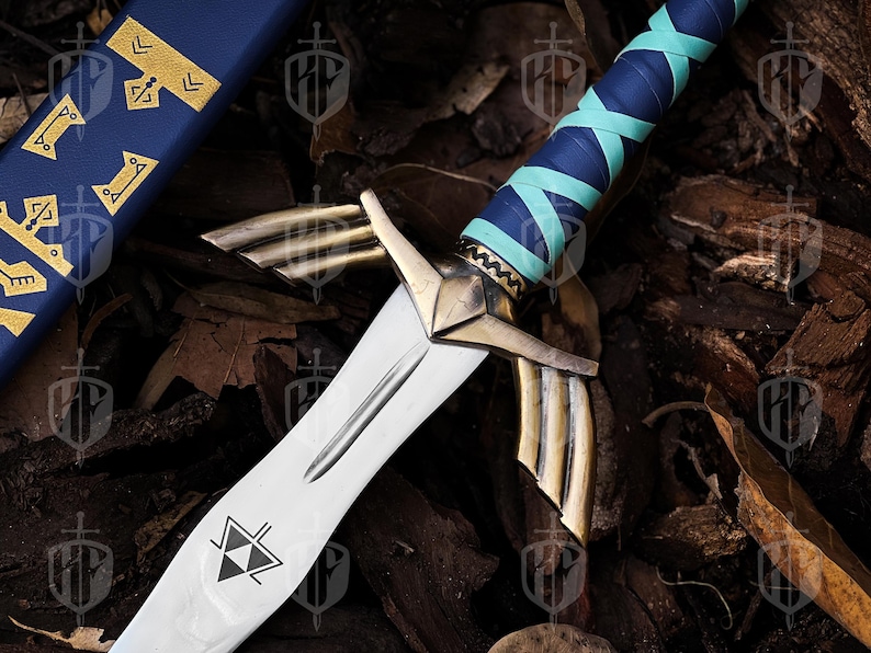 Pode incluir: Uma espada de fantasia com uma l&acirc;mina prateada e detalhes dourados. O punho &eacute; envolto em couro azul e verde-azulado. A bainha &eacute; azul com elementos decorativos dourados. A espada apresenta um s&iacute;mbolo triangular preto e branco na l&acirc;mina.