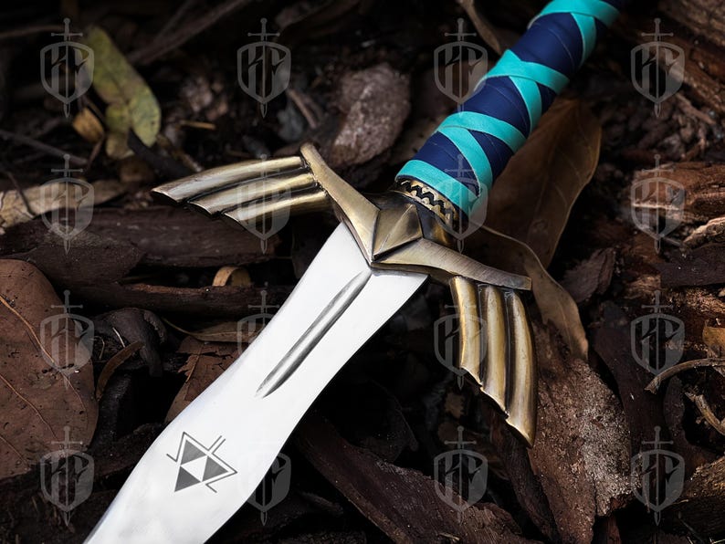 Pode incluir: Uma espada decorativa com uma l&acirc;mina prateada e detalhes dourados. O punho &eacute; envolto em couro azul e verde-azulado. A l&acirc;mina apresenta um design triangular. A espada est&aacute; sobre um fundo de madeira e folhas.