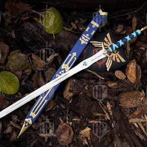 Pode incluir: Uma espada de fantasia com uma l&acirc;mina branca e detalhes dourados, repousando sobre uma cama de folhas e madeira. A espada tem uma empunhadura azul e dourada, com uma bainha a condizer e um escudo com um emblema dourado.