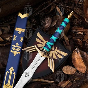 Pode incluir: Espada, escudo e bainha de fantasia. A espada tem uma l&acirc;mina prateada, uma guarda dourada e uma empunhadura enrolada em azul turquesa e marinho. O escudo &eacute; preto com um emblema dourado. A bainha &eacute; azul com detalhes dourados.