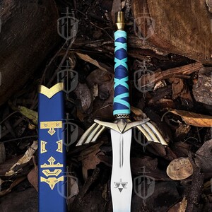 Pode incluir: Uma espada de fantasia com uma l&acirc;mina prateada e detalhes dourados. O punho &eacute; envolto em azul e turquesa, e a bainha &eacute; azul com detalhes dourados. A espada repousa sobre uma cama de folhas e madeira.