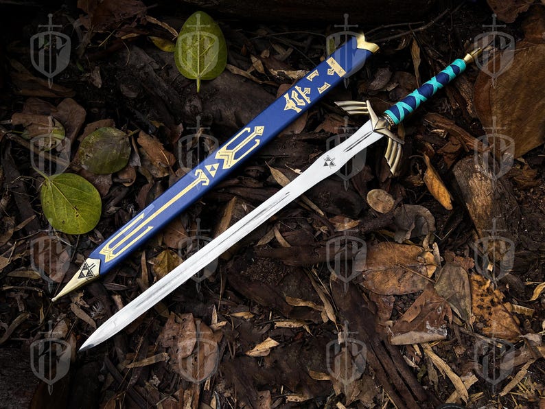 Pode incluir: Uma espada prateada com uma guarda dourada e uma pega enrolada em azul e azul-turquesa, repousando sobre uma cama de folhas e galhos. A espada tem uma bainha azul a condizer com detalhes dourados. A l&acirc;mina tem um emblema triangular perto da guarda.